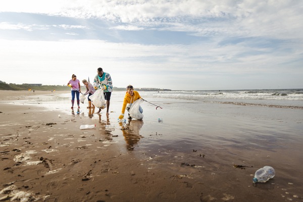 Collecting rubbish off a beach. Plastic containers, bottles in their bag. They are using a mechanical grabber. Three women and a man working together